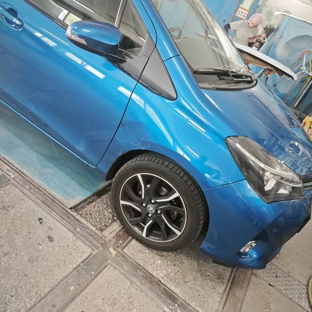 Blauer Kleinwagen in der Werkstatt mit beschädigter Front und Kotflügel