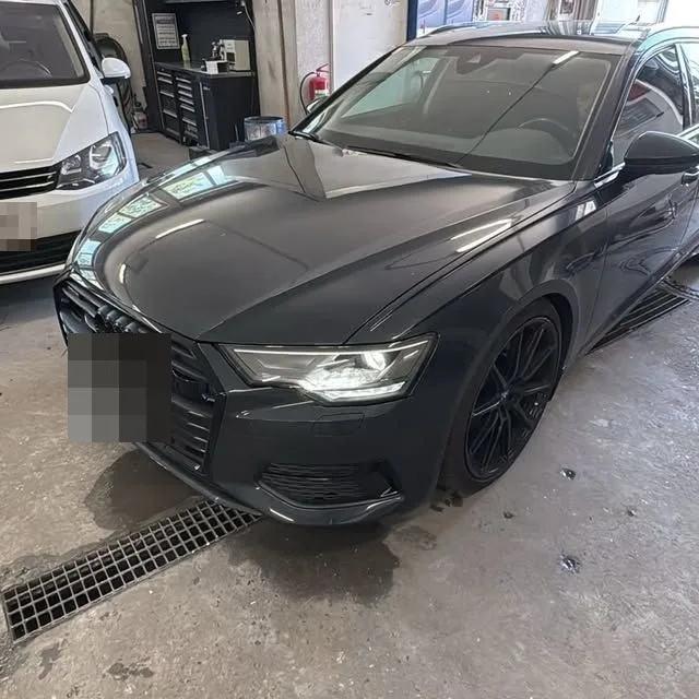 Dunkelgrauer Audi A6 mit schwarzen Felgen in der Werkstatt, daneben ein Werkzeugwagen