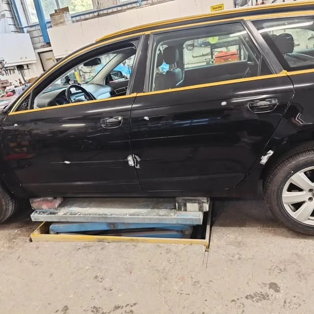 Schwarzer Kombi auf der Hebebühne, Fenster und Türkanten mit gelbem Band abgeklebt